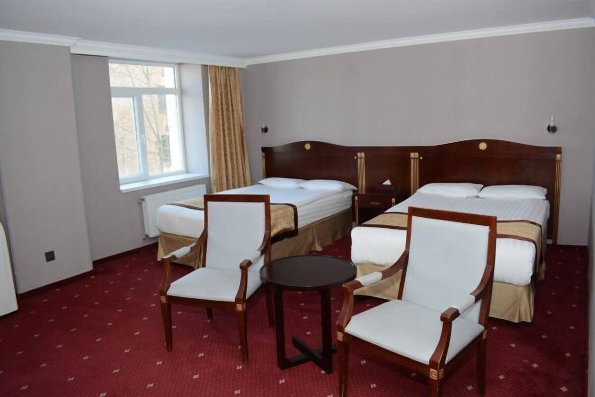 Hotellihuone, jossa on kaksi sänkyä, pieni pyöreä pöytä ja kaksi tuolia.