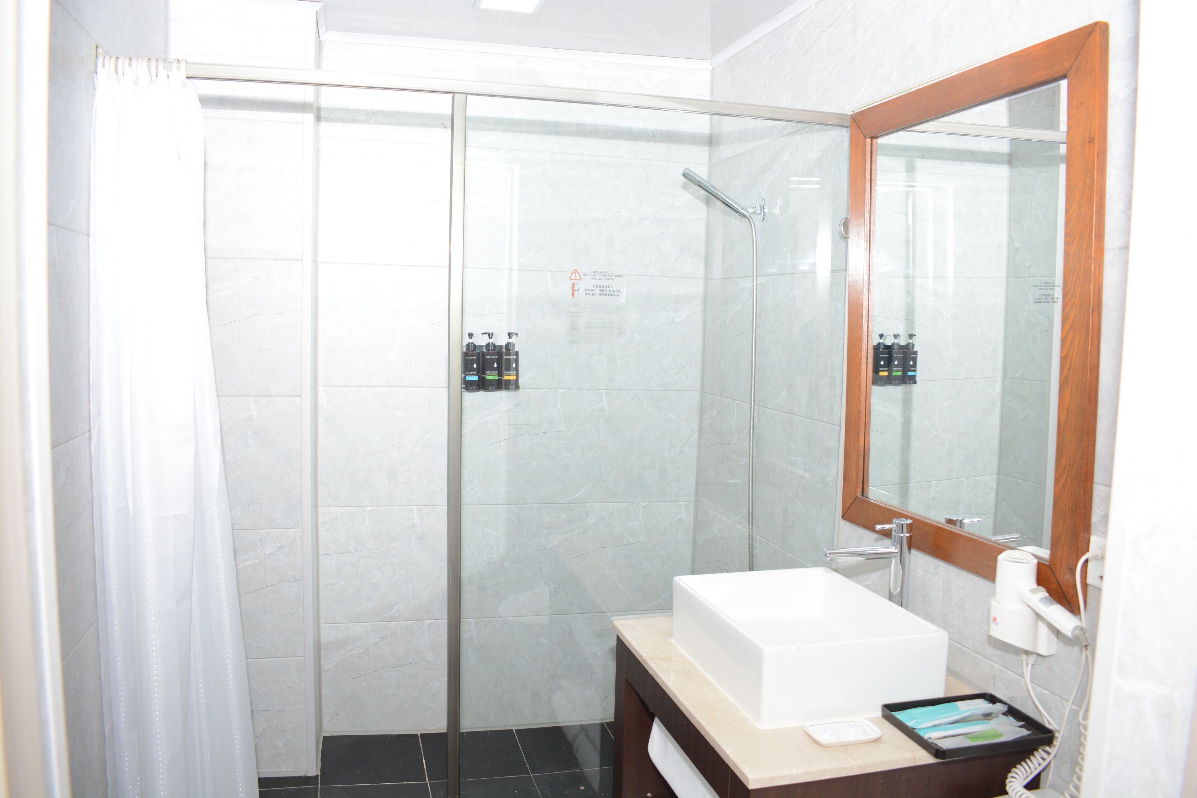 Un baño moderno con ducha de vidrio, un lavabo blanco y un espejo con marco de madera.