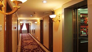 A hotel hallway with a patterned carpet, wall sconces, and a door with a frosted glass window. - White House Hotel (Ulaanbaatar)