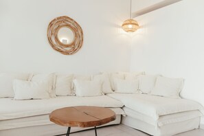 Un canapé d’angle blanc, une table basse ronde en bois, une œuvre d’art murale en fibres tressées et un luminaire suspendu.