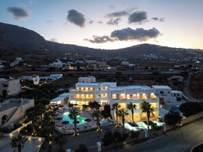 A resort with a swimming pool, multiple buildings, and a mountainous backdrop. - Casa Vitae Suites (Santorini)