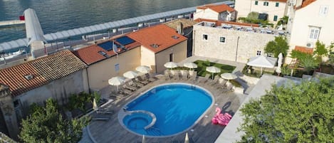 Una piscina con sillas de descanso y sombrillas, rodeada de edificios y una orilla de agua.