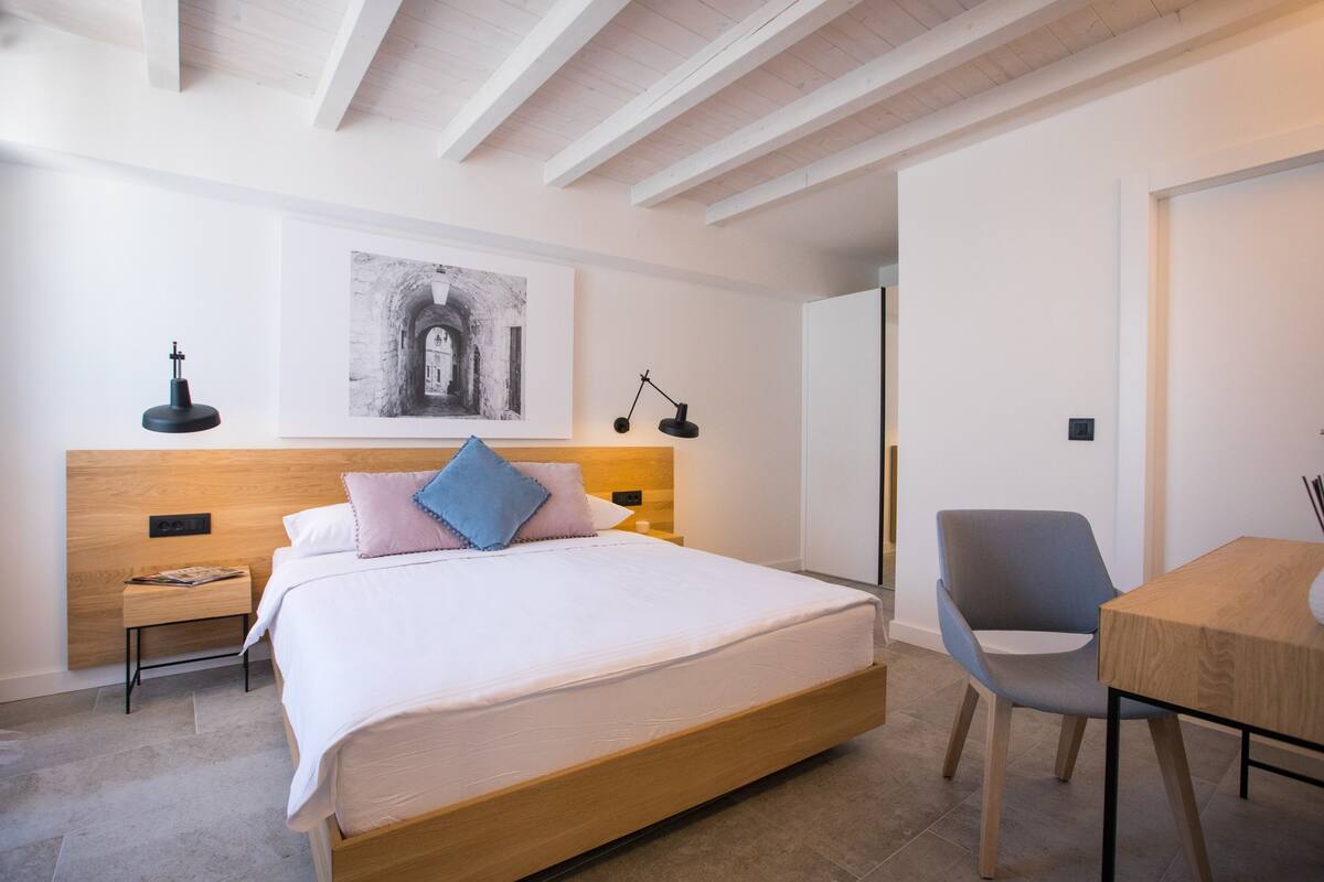 Een moderne slaapkamer met een houten bed, nachtkastje, bureau en stoel.