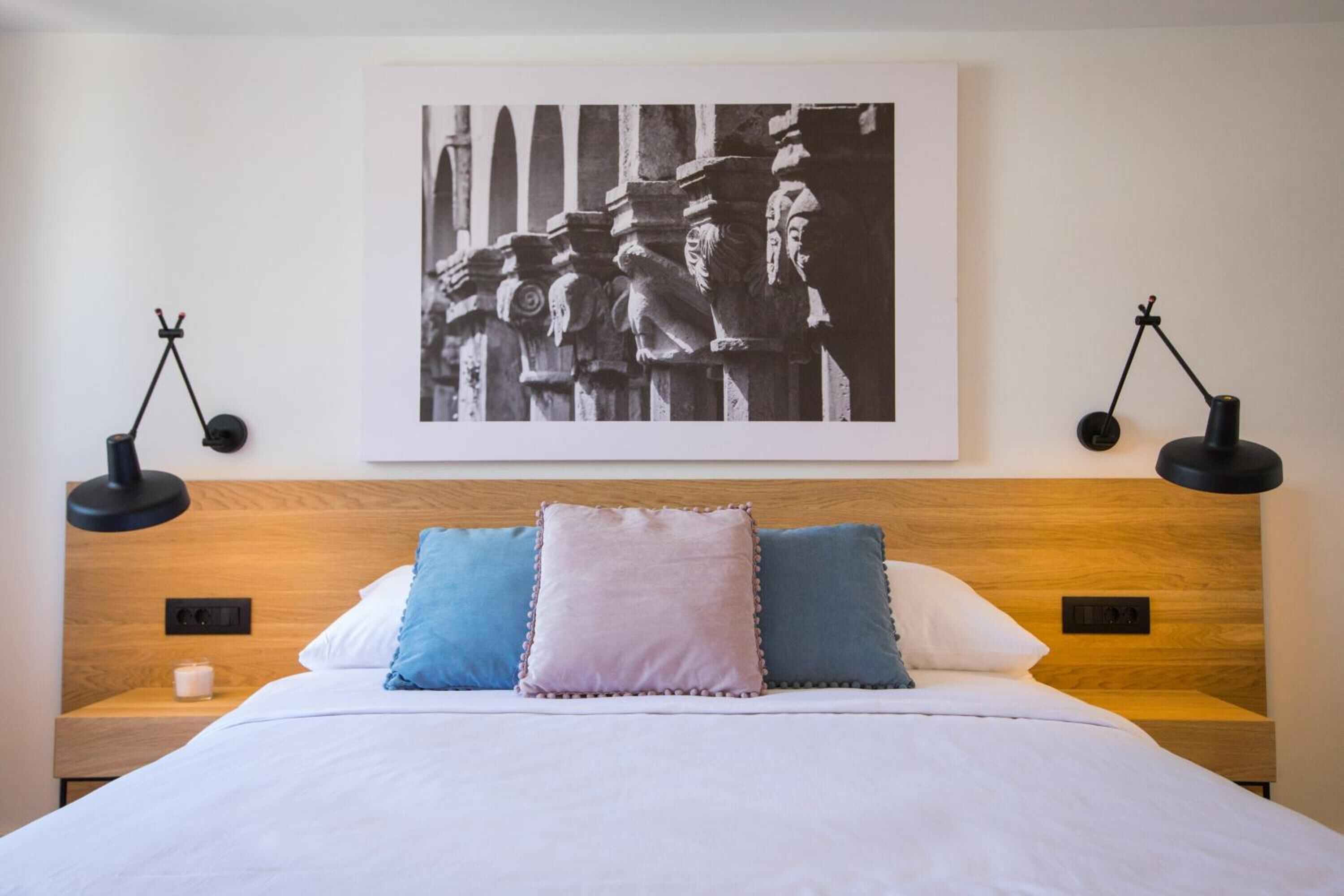 Een net opgemaakt bed met een houten hoofdbord, twee bedlampjes en een zwart-wit foto in een lijst aan de muur.