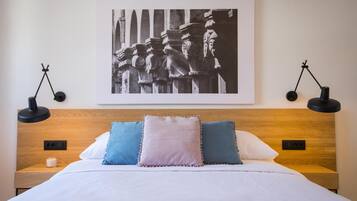 Een net opgemaakt bed met een houten hoofdbord, twee bedlampjes en een zwart-wit foto in een lijst aan de muur.