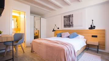 Un dormitorio moderno con cabecera de madera, cama con manta rosa, mesita de noche con lámpara y un taburete pequeño.