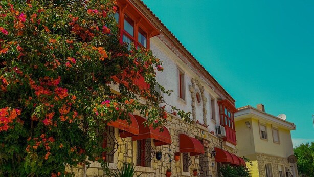 A stone building with red awnings, outdoor seating, and a cobblestone street. - Narcicegi Alacati (Cesme)