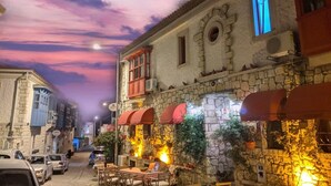 A stone building with a restaurant patio, outdoor seating, and a street view at dusk. - Narcicegi Alacati (Cesme)