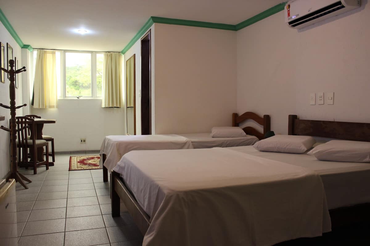 A hotel room with two beds, a wooden chair, a desk, and a window with curtains.
