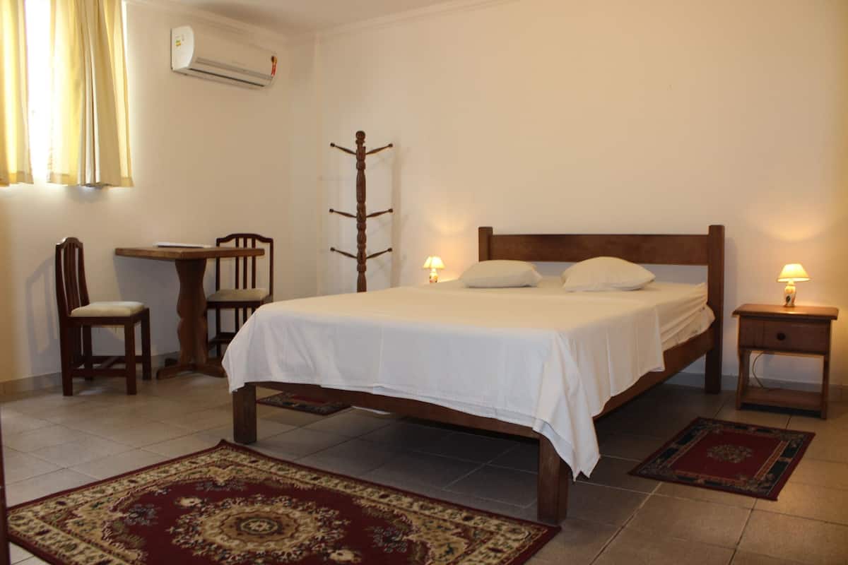 A bedroom with a wooden bed, two bedside tables with lamps, a chair, a desk, and a red patterned rug.