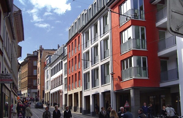 A street with modern buildings, including a red building with balconies and a sign for a coffee shop. - The Apartment Downtown (Mainz)