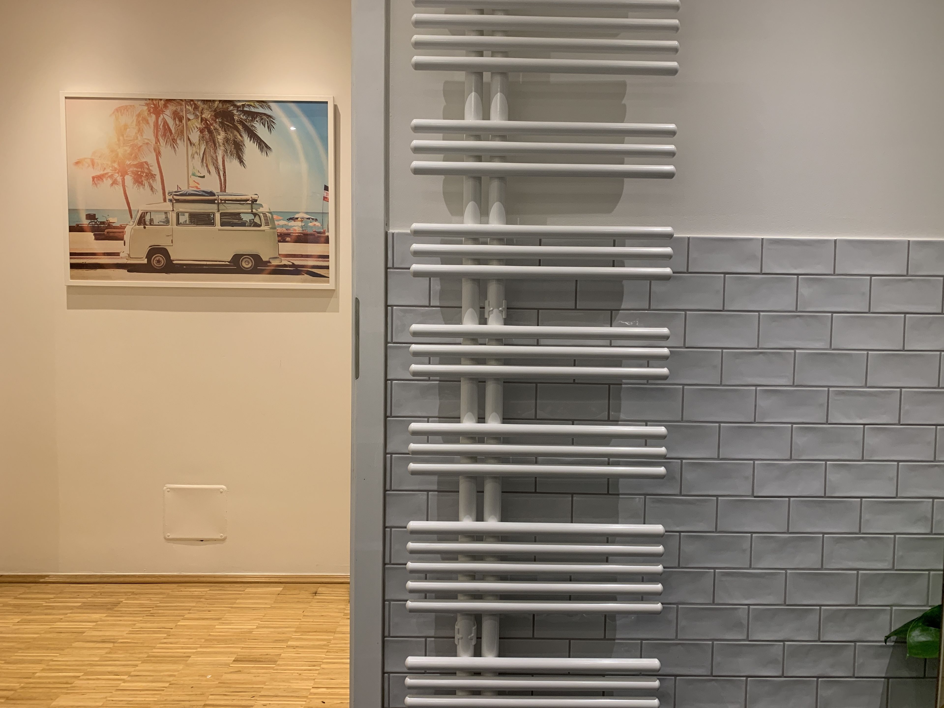 Ein Zimmer mit Fliesenwand, einem weißen Heizkörper und einem gerahmten Bild eines Fahrzeugs an der Wand.