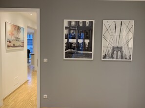 A hallway with three framed artworks on the wall, a door leading to another room, and a light switch. - The Apartment Downtown (Mainz)