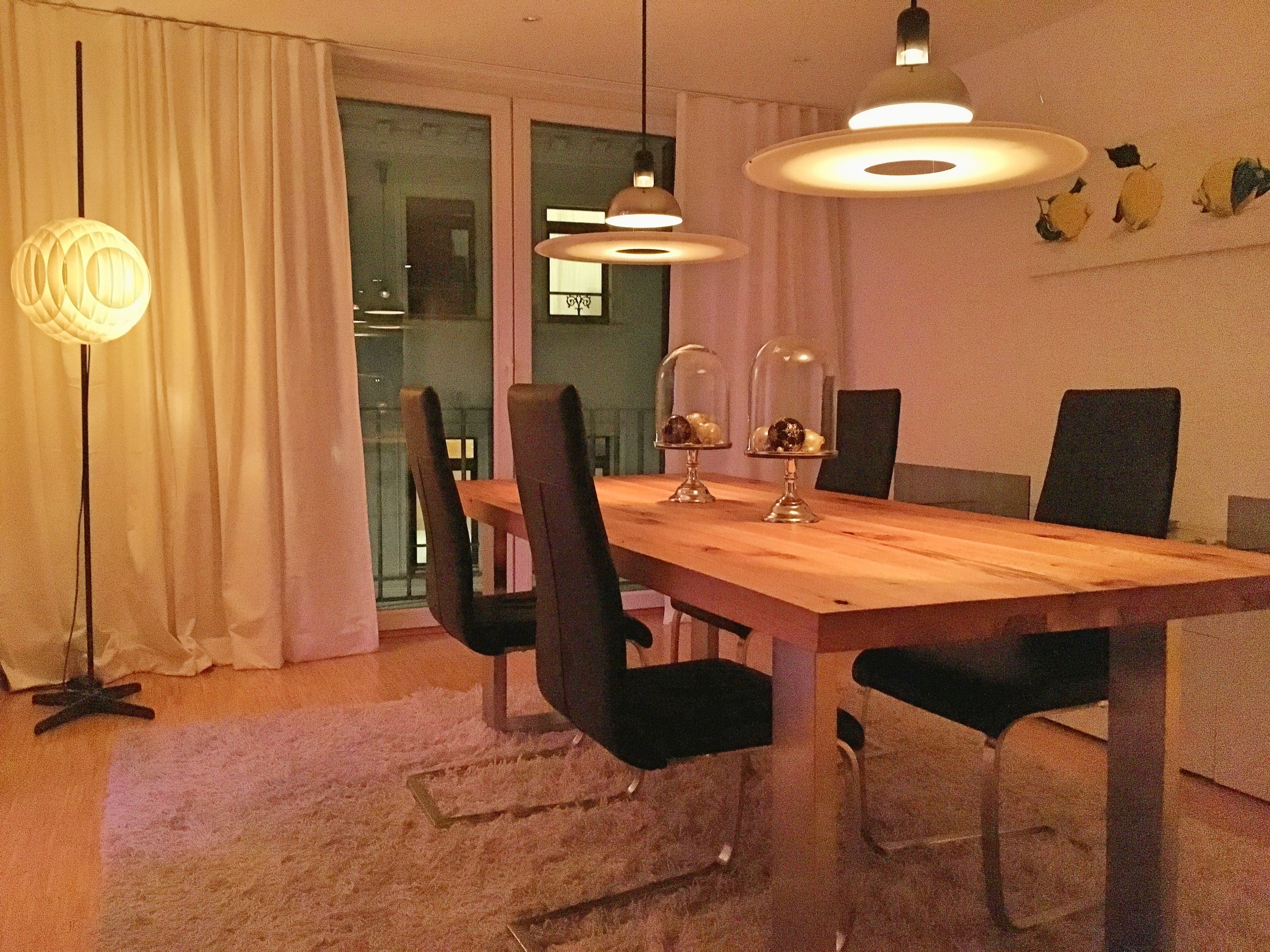 Un espace repas avec une table en bois, des chaises noires et des luminaires suspendus.