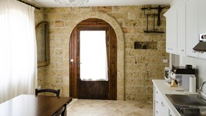 Una cocina con pared de piedra, puerta de madera y armarios blancos.