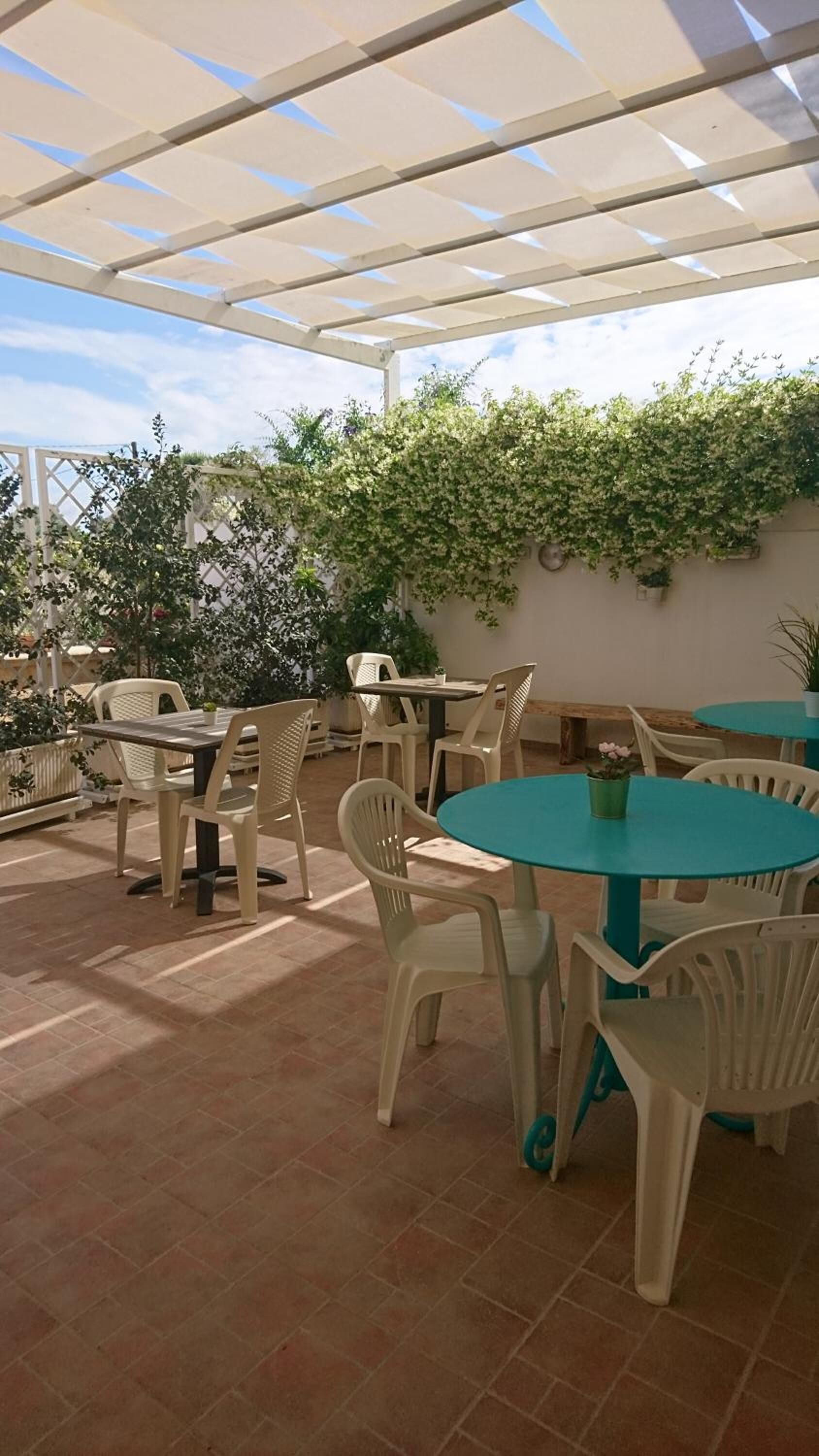 An outdoor patio with white plastic chairs and tables, a covered area with a white roof, and green plants on the walls.