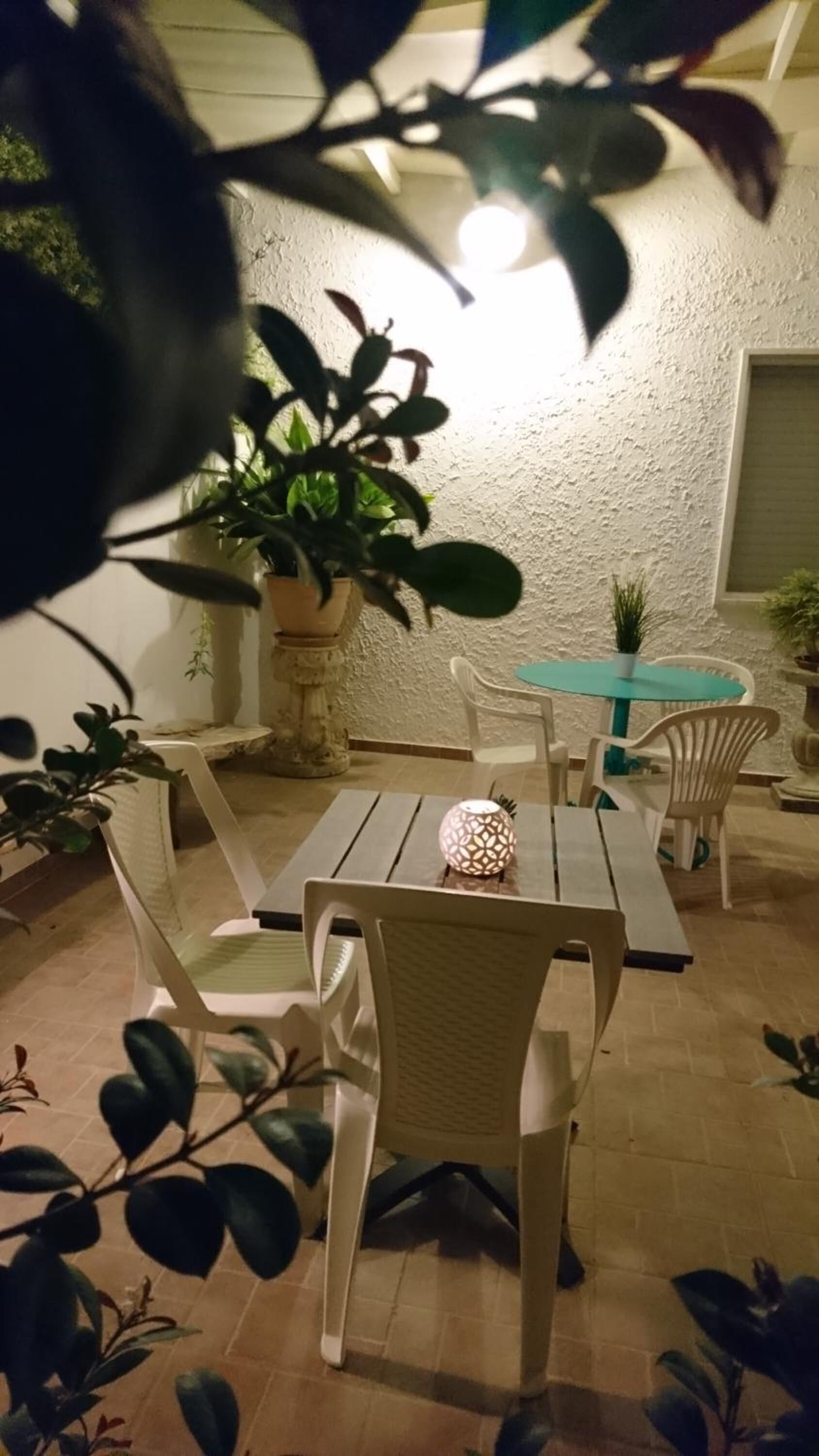 A patio area with white wicker chairs, a turquoise table, and potted plants.