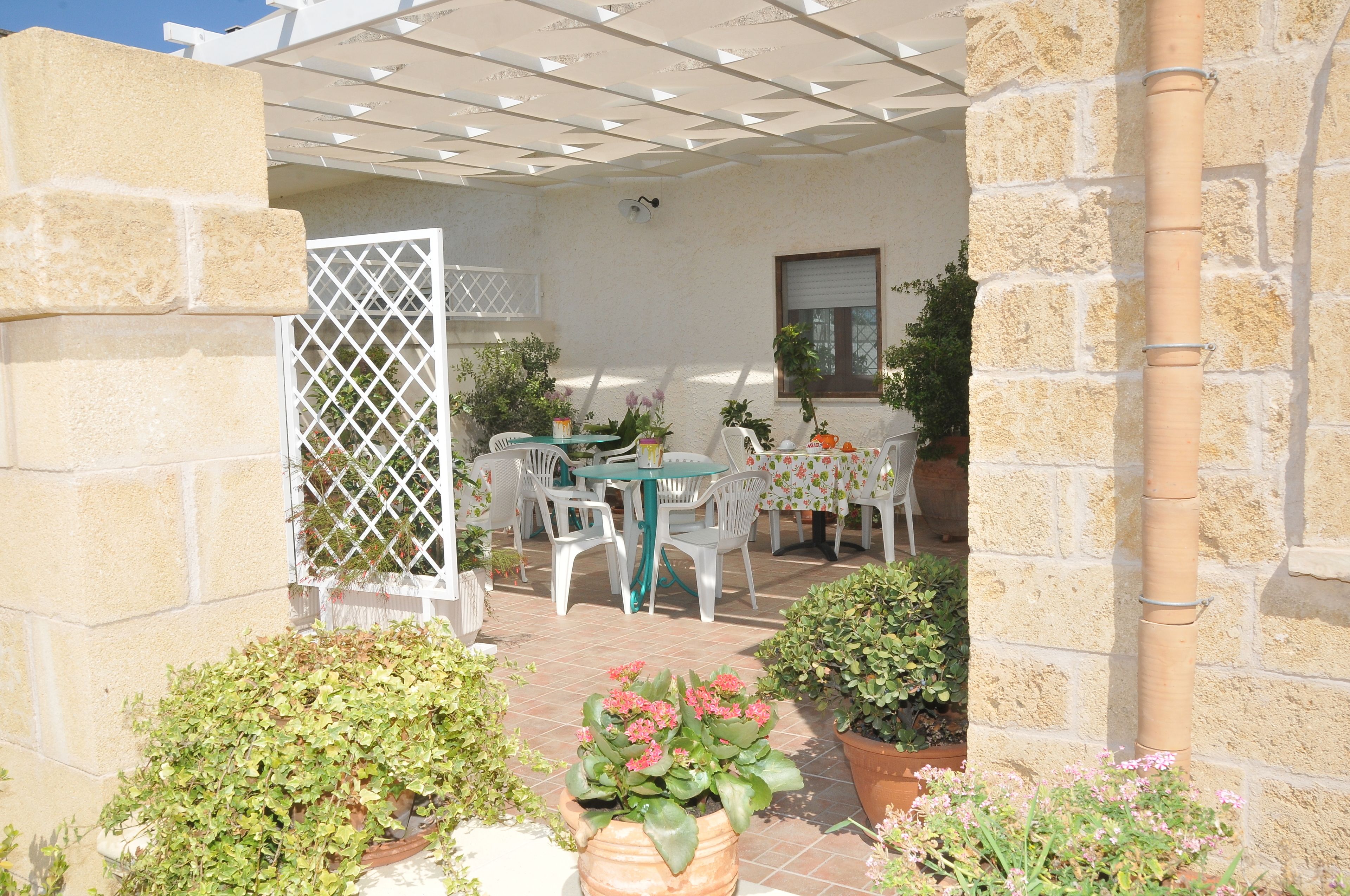 Eine Terrasse im Freien mit Tisch und Stühlen, umgeben von Kübelpflanzen und einem weißen Zaun.