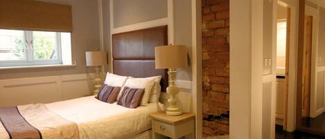 A neatly arranged bedroom with a bed, bedside lamps, a window with a blind, and a brick wall.