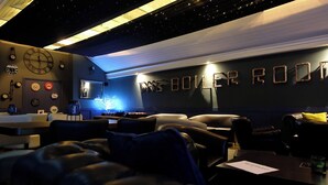 A cozy lounge area with leather seating, a bar area, and a wall with clocks and the text "THE BOILER ROOM". - The Lawns Hotel (Derby)