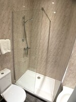 Un baño moderno con ducha envuelta en vidrio, un inodoro blanco y una puerta de vidrio para la ducha.