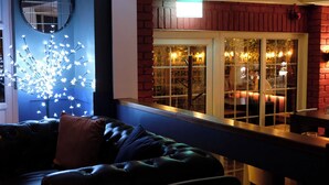 A dark leather sofa with a cushion, a round mirror, and a decorative light installation. - The Lawns Hotel (Derby)