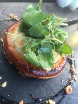 A dessert with a glazed base, topped with green leaves and thin stems, on a dark slate plate.