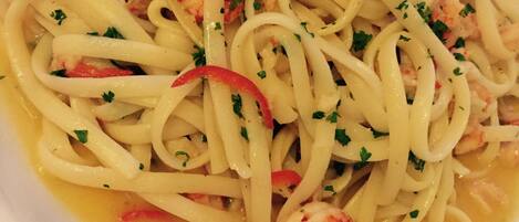 A plate of pasta with shrimp and red bell peppers, garnished with chopped parsley.