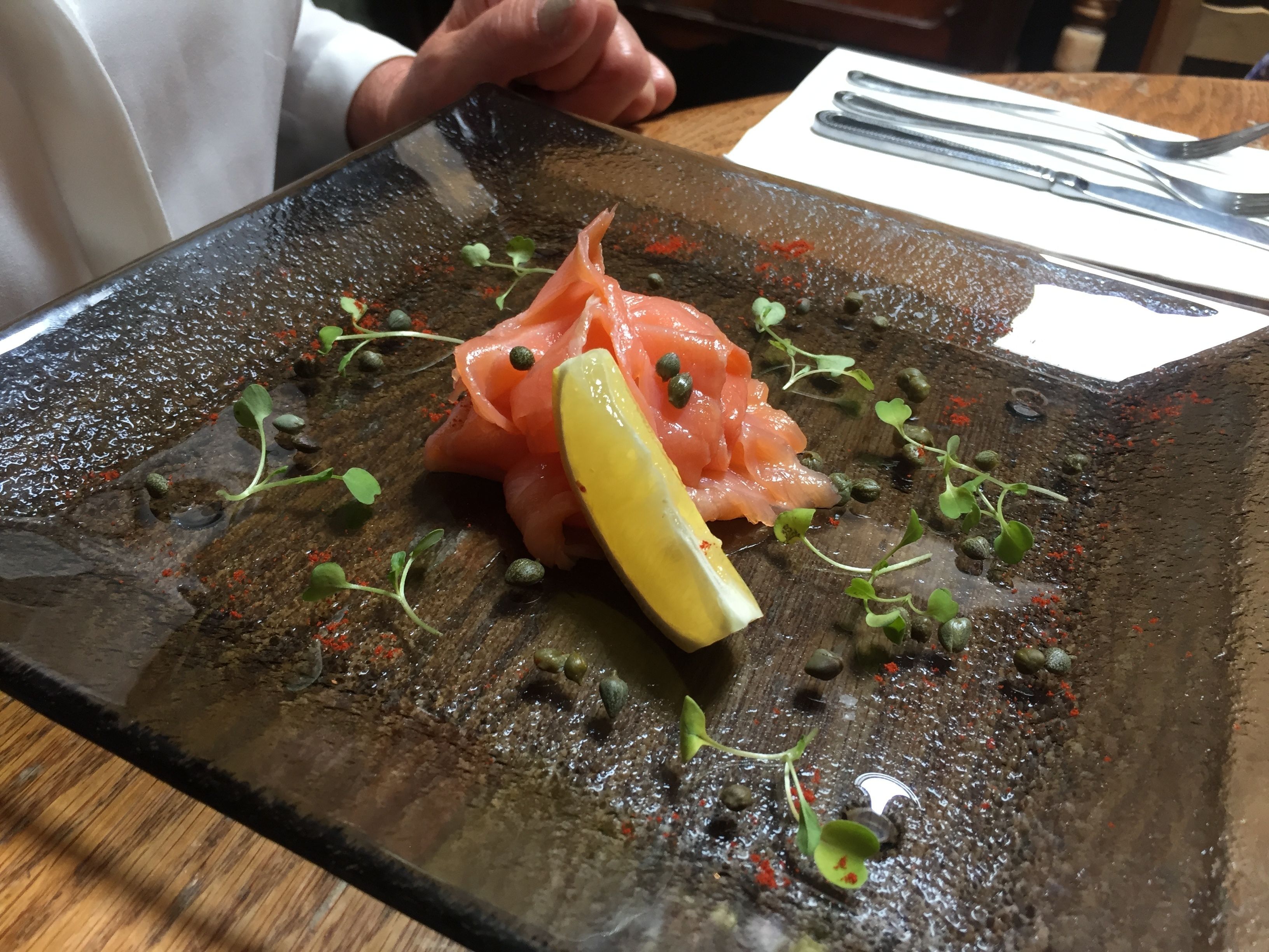 A plate of food with salmon, capers, and a lemon wedge.