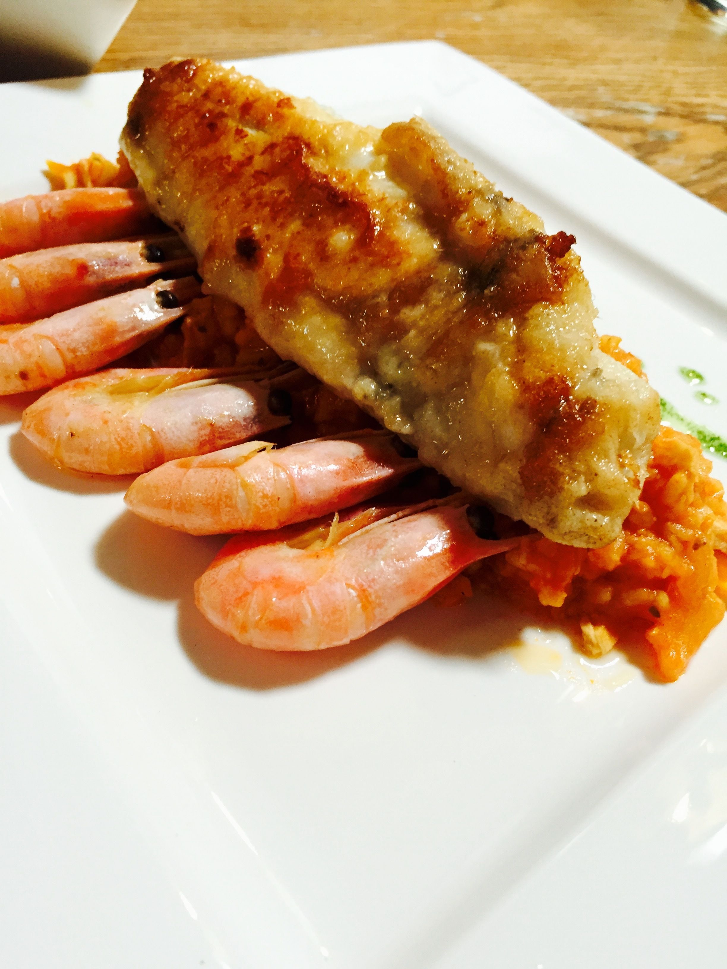 A plate with a grilled fish fillet and several cooked shrimp.