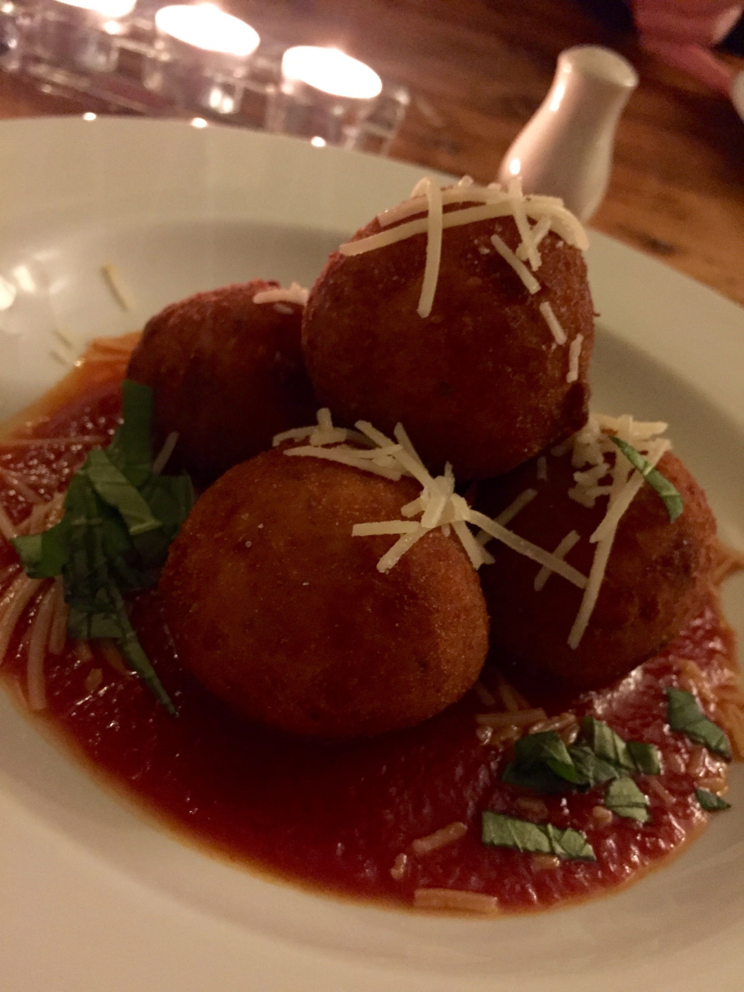 A plate of food with round, breaded items topped with grated cheese and garnished with herbs, served on a white plate with a red sauce.