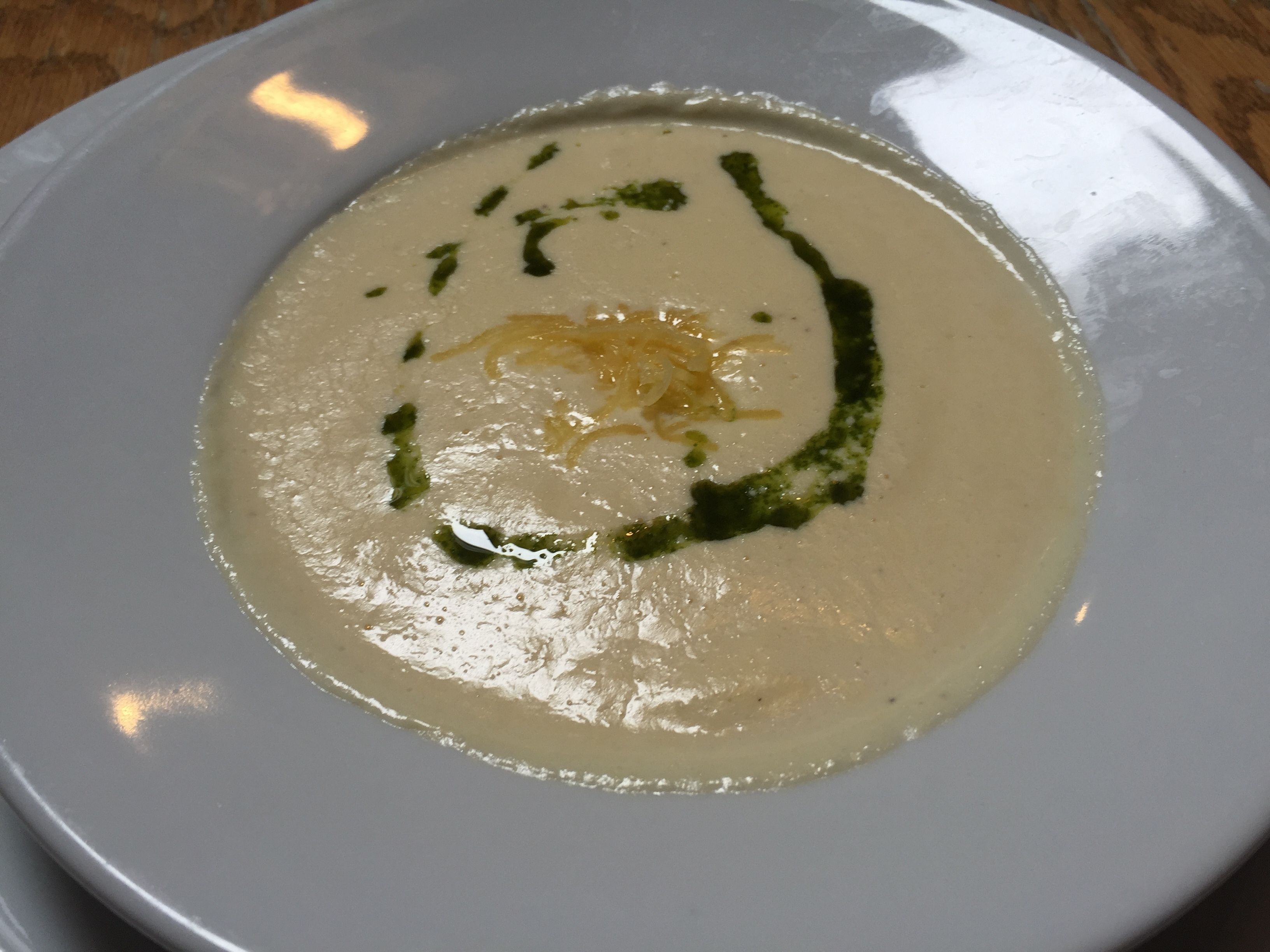 Un plato blanco con crema de sopa, adornado con hierbas verdes y queso rallado.