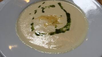 Un plato blanco con crema de sopa, adornado con hierbas verdes y queso rallado.