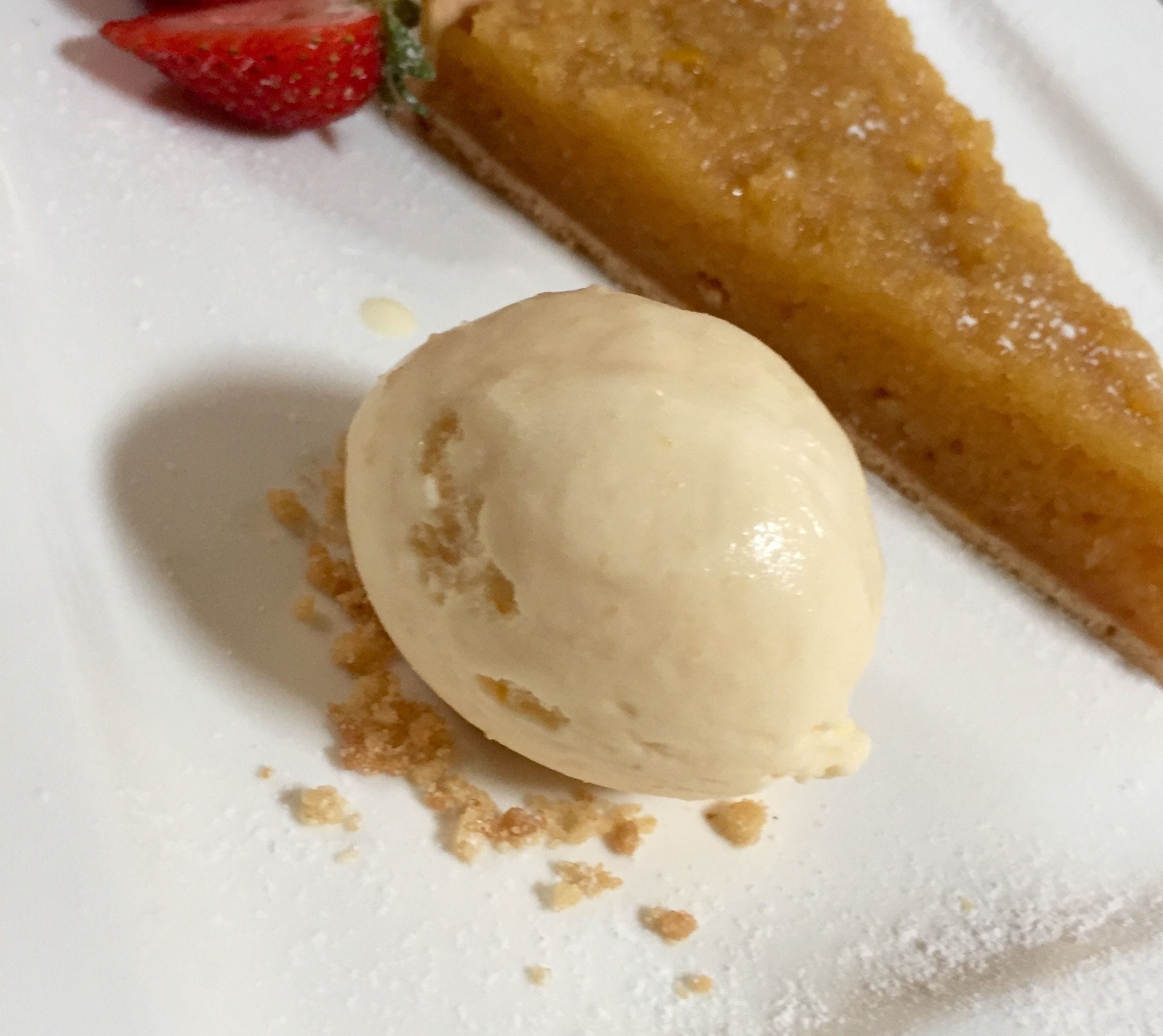 Un plato de postre con una bola de helado, una porción de pastel y una fresa.
