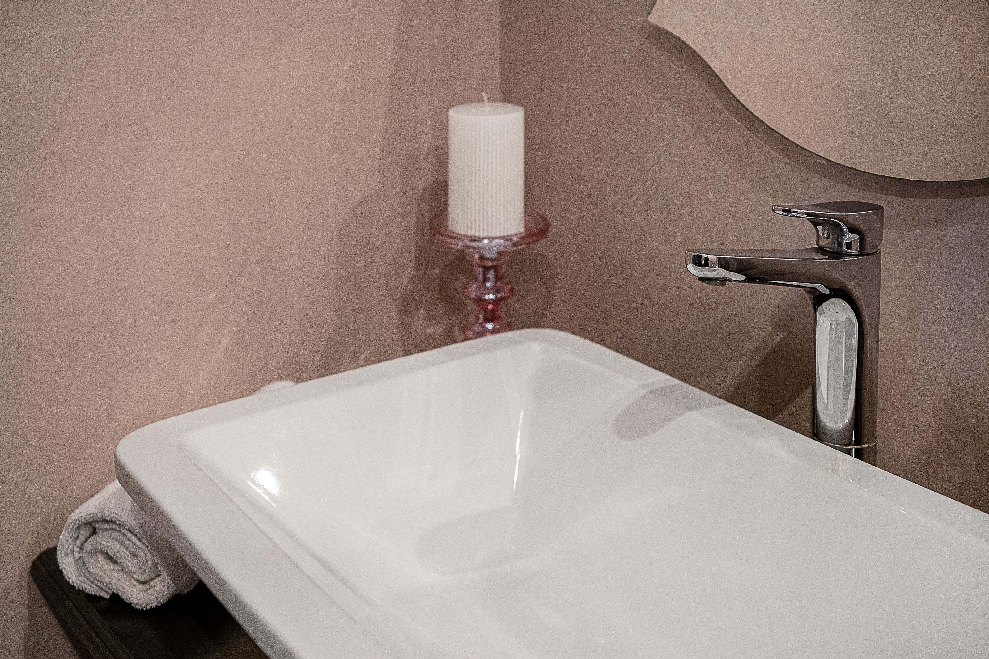 Un baño con un lavamanos blanco, un grifo plateado y una vela blanca sobre un portavelas rosa.