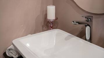 Un baño con un lavamanos blanco, un grifo plateado y una vela blanca sobre un portavelas rosa.