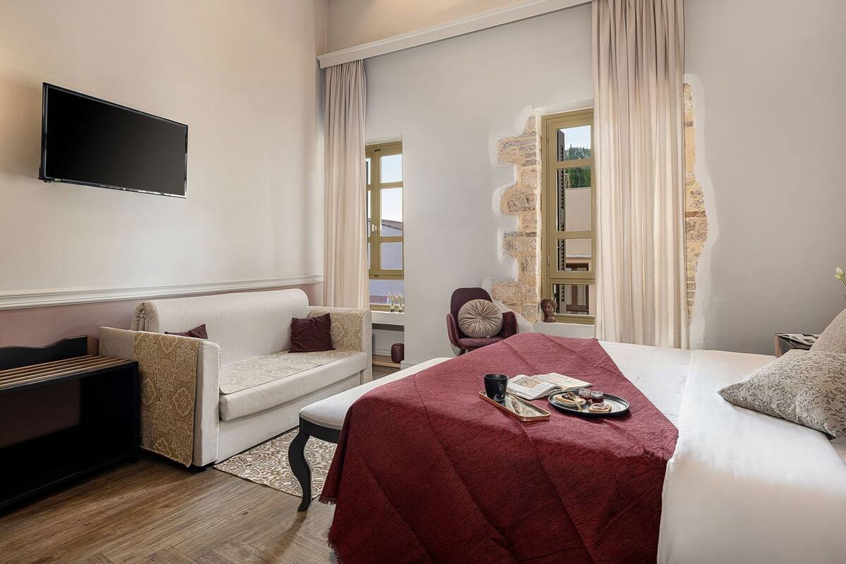 A hotel room with a bed, a sofa, a chair, a TV, and a window with curtains.