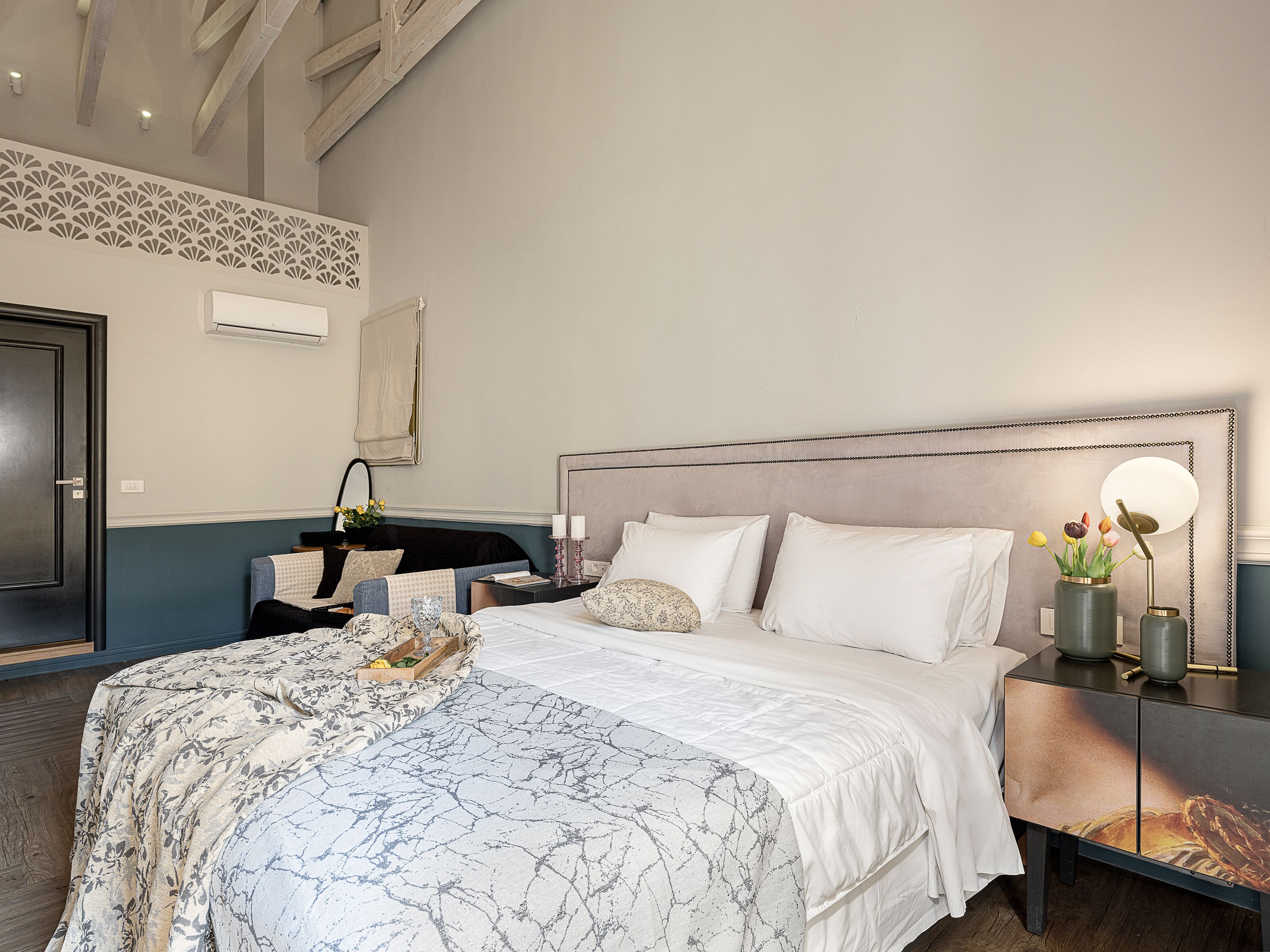 A hotel room with a large bed, a bedside table with a lamp, a dresser, and a decorative wall panel.