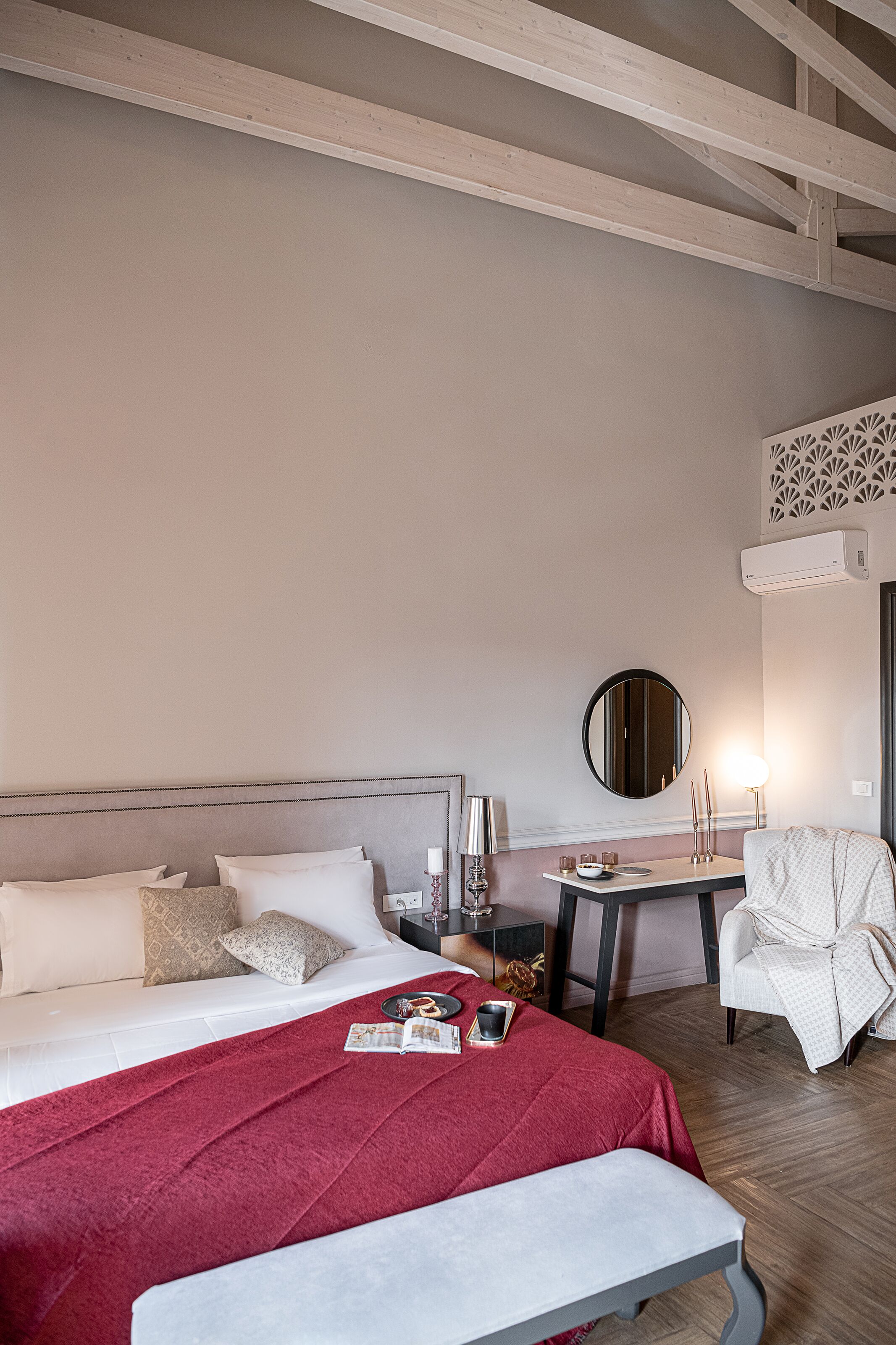 A hotel room with a bed, bedside table, chair, and a small table with a lamp.