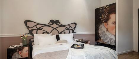 A neatly made bed with a decorative headboard, a bedside table with a vase of flowers, and a large framed artwork on the wall.