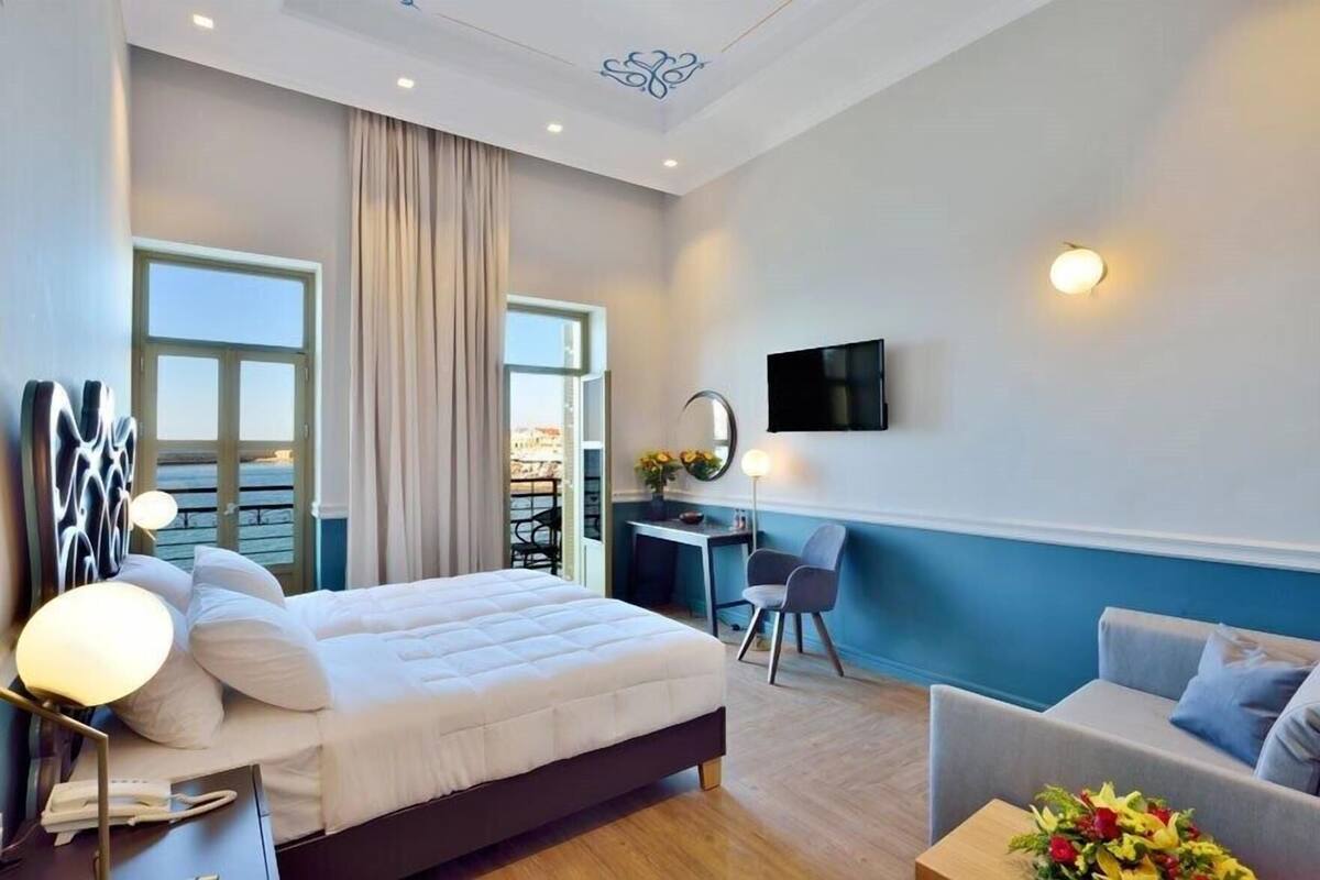 A modern hotel room with a bed, desk, chair, and a TV on the wall.