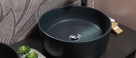 A modern bathroom with a round black sink, a faucet, and a small plant on a tray.