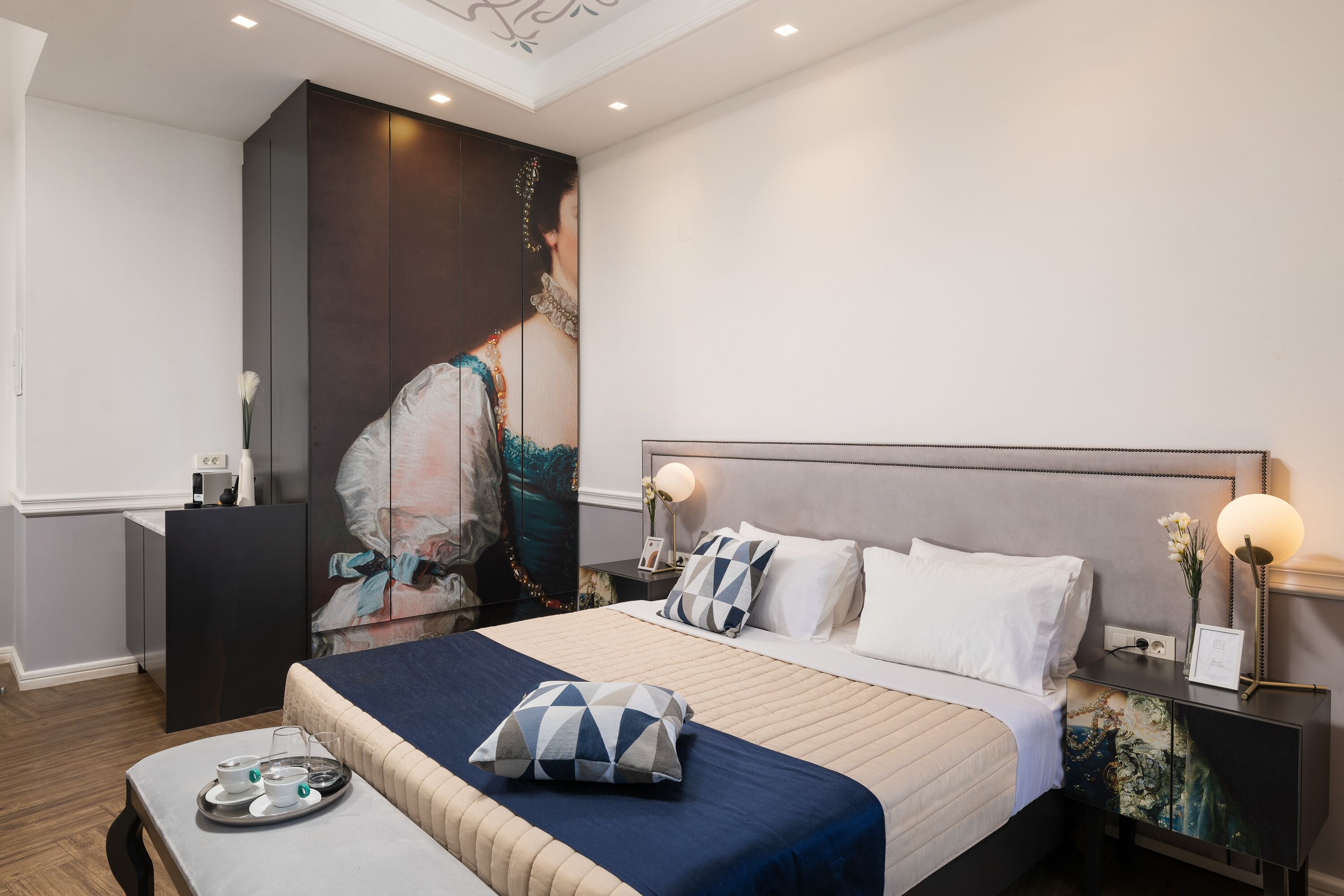 A modern hotel room with a large bed, a desk, and a painting on the wall.