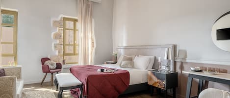 A well-lit bedroom with a large bed, a bedside table with a lamp, a chair, and a desk with a mirror.