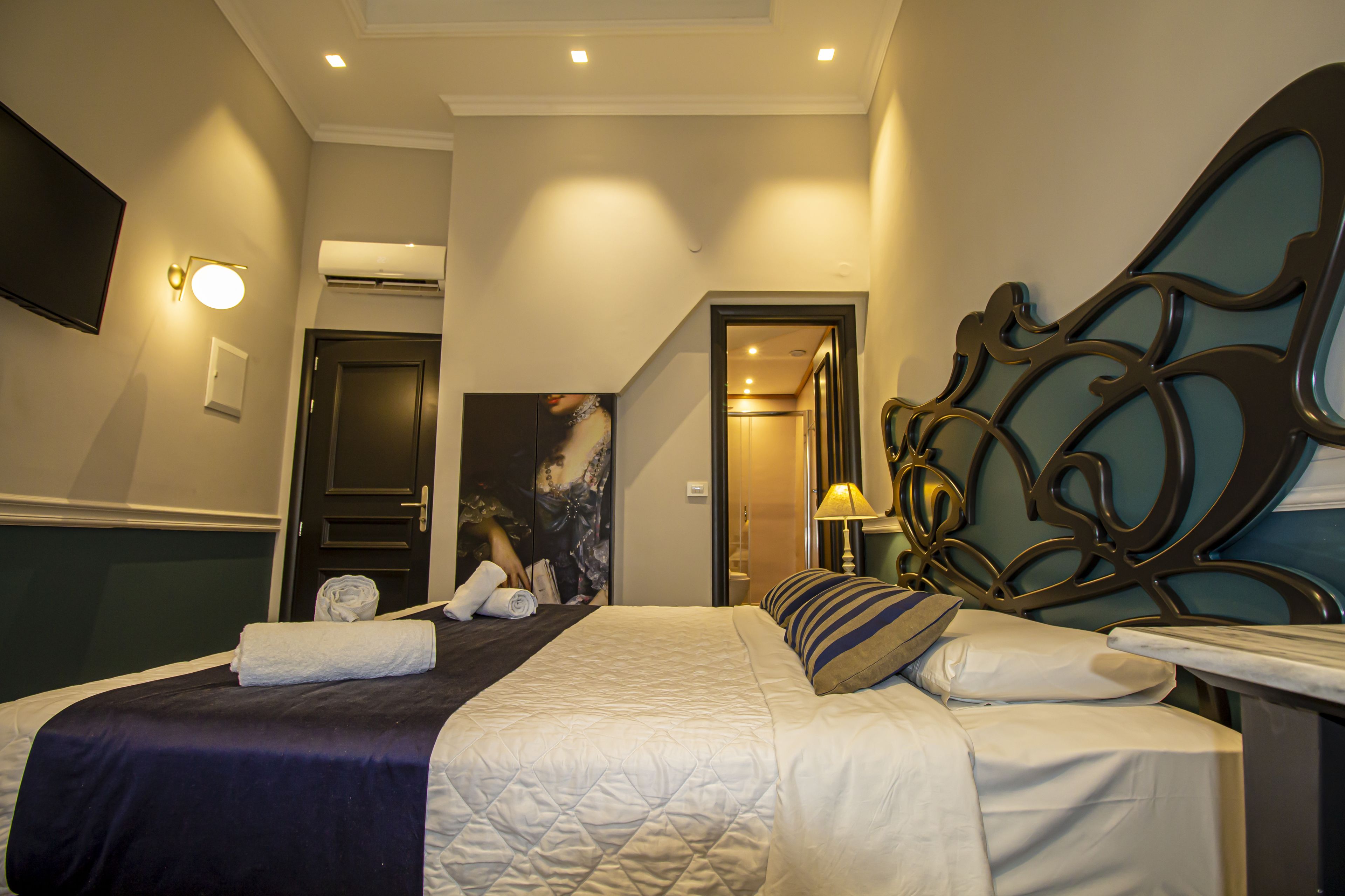 A hotel room with a bed, a flat-screen TV, an air conditioning unit, and a painting on the wall.