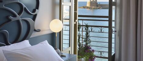A hotel room with a bed, a nightstand, a lamp, and a view of a lighthouse through an open balcony door.
