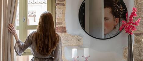 A room with a large window, a mirror, a vase with flowers, and a red chair.