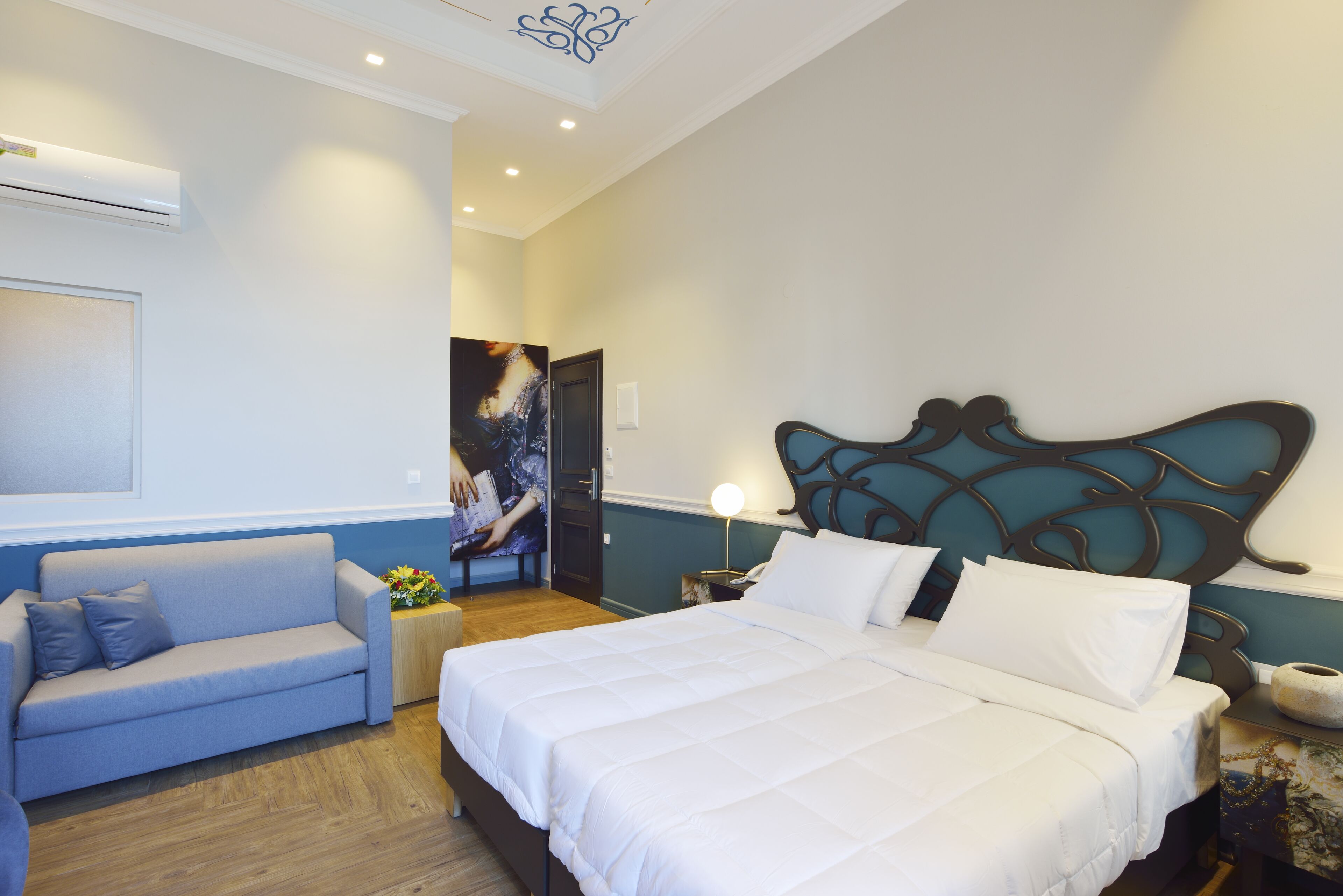 A bedroom with a bed, a sofa, a nightstand, a lamp, and a wall-mounted air conditioner.