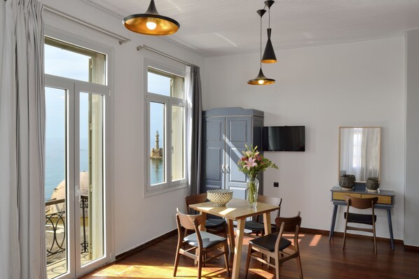 A dining area with a table and chairs, a vase with flowers, and a view of the sea through large windows.