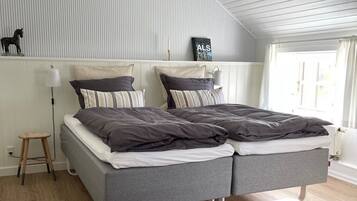 Un dormitorio moderno con techo estilo loft, una cama gris con almohadas a rayas, un taburete pequeño y un radiador.